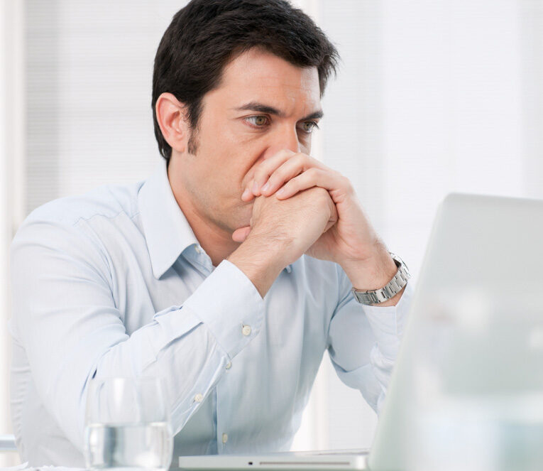 Man looking at computer, feeling stressed, experiencing self-doubt and imposter feelings