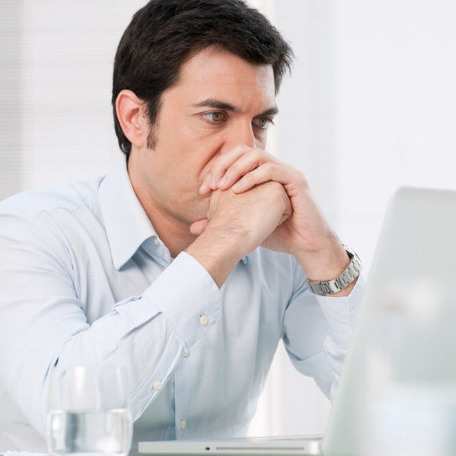 Man Struggling with Imposter Syndrome Man looking at computer, feeling stressed, experiencing self-doubt and imposter feelings
